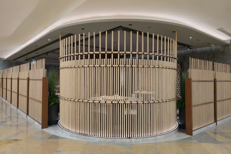 A retail pavilion enclosed in curved timber battens, lit from a cove at its base, standing on a stone floor.
