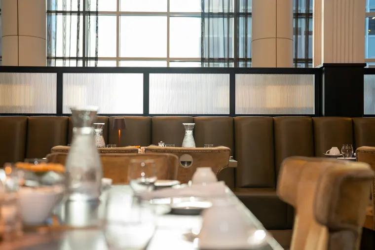 A restaurant interior: tan leather banquettes, a laid table and dark steel glazing behind.
