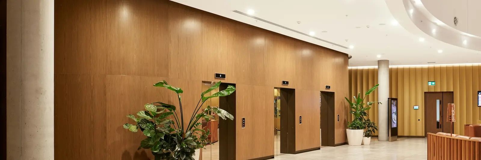 A commercial lobby: a curved timber-clad wall, a curved slatted reception counter, recessed lighting and a large-format stone floor.