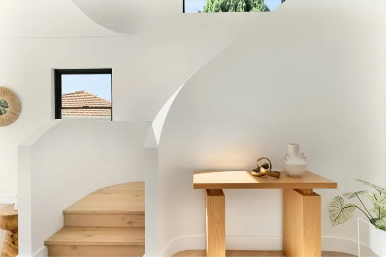 A curved plastered stair rising against a white wall, with a solid timber console beneath the arch of its underside.