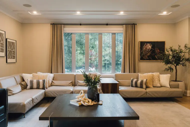 A long living room in cream tones: a full-length corner sofa, an olive tree and a cove-lit ceiling.