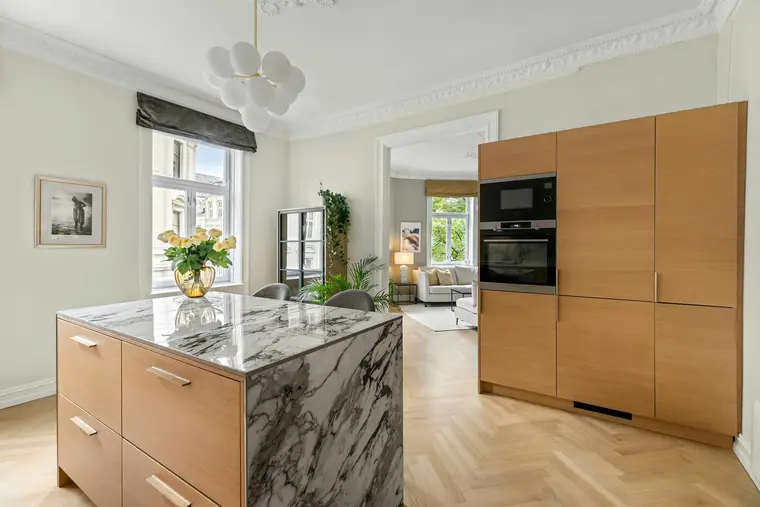 A kitchen island in veined marble with oak fronts and a full-height oak unit, on a herringbone floor.