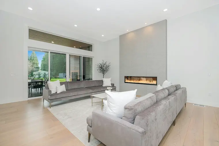 A living room with a linear fireplace set into a plastered chimney breast, opening through full-height glazing onto a garden.