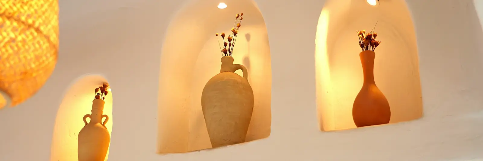 Three arched niches cut into hand-finished lime plaster, each holding a terracotta vessel, lit from within.