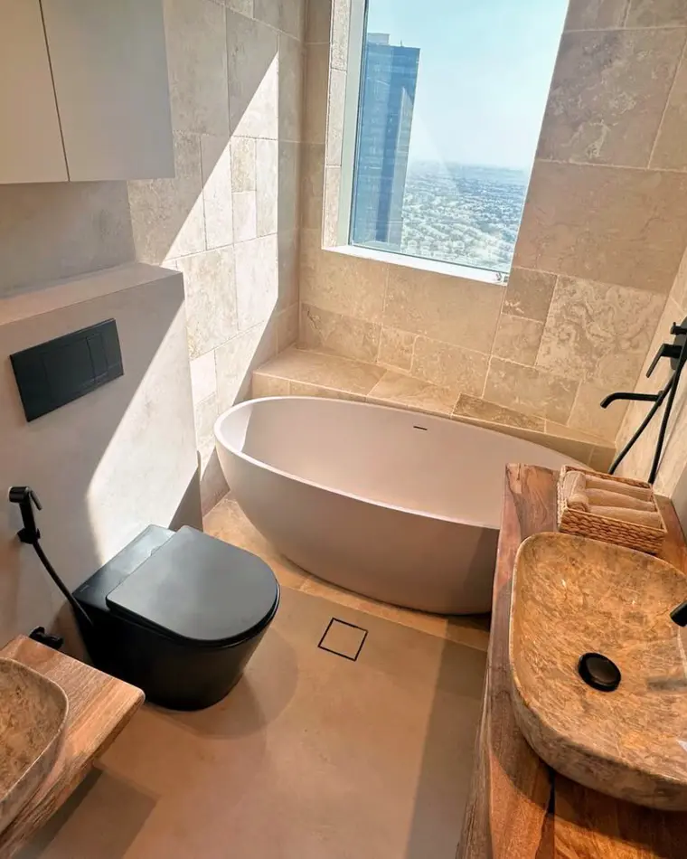 Bathroom in JLT: travertine walls, a freestanding bath, a live-edge timber vanity and a city view.