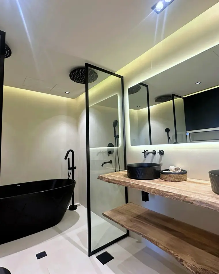 Bathroom in JBR: black freestanding bath, walk-in shower behind glass, a live-edge timber double vanity.