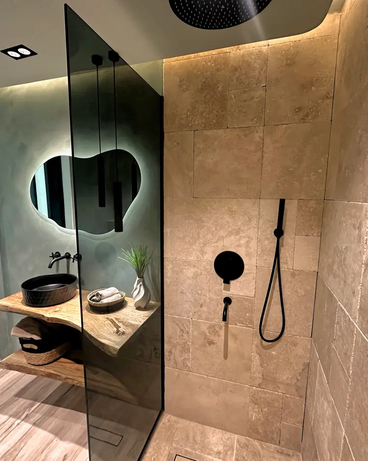 Bathroom in JLT: travertine floor to ceiling, matt black fittings, a linear drain and frameless smoked glass.