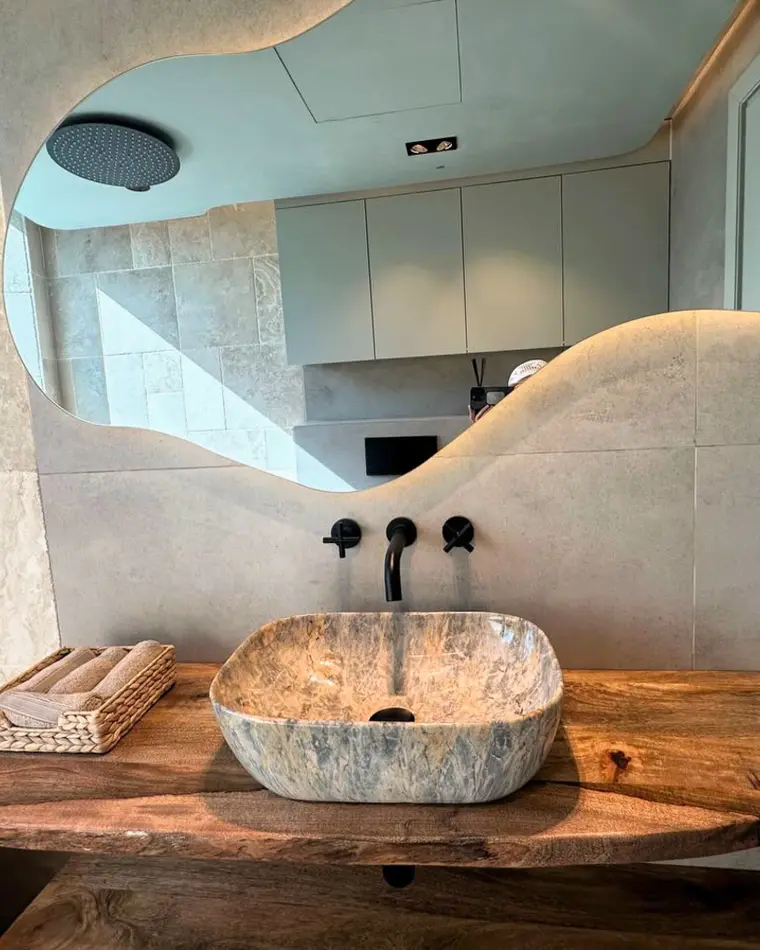 Bathroom in JLT: stone vessel basin on a live-edge timber shelf under an organic backlit mirror.