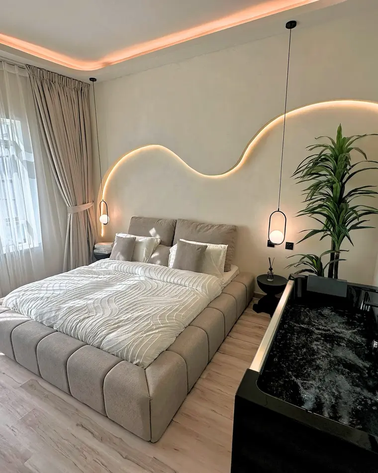 Bedroom in JLT: upholstered bed under a serpentine cove light, sheer curtains and a black inset jacuzzi.