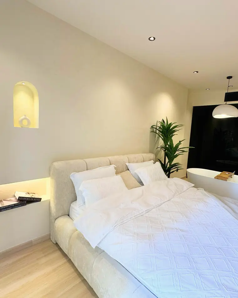 Bedroom in JBR: a wide bed between backlit niches, on pale oak flooring.