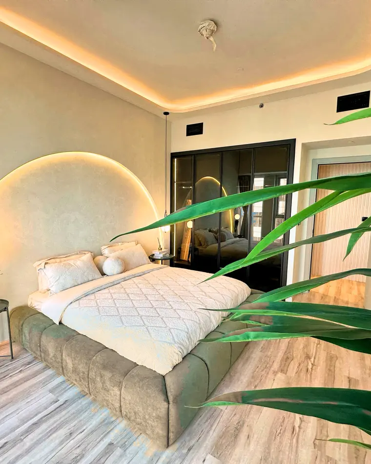 Bedroom in Business Bay: arched backlit headboard, smoked-glass wardrobes and an indoor palm.