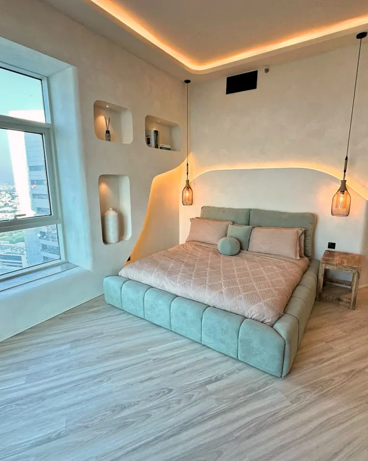 Bedroom in TECOM: sage upholstered bed, wall niches and a window onto the towers.