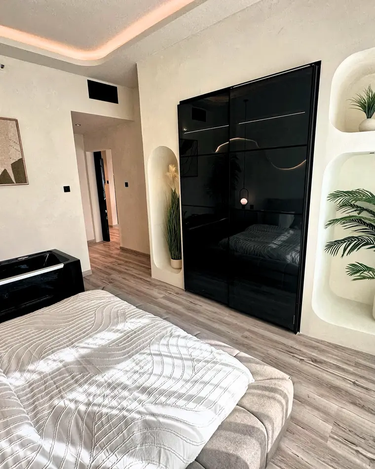 Bedroom in JLT: a bed facing planted niches and a black gloss wardrobe wall.
