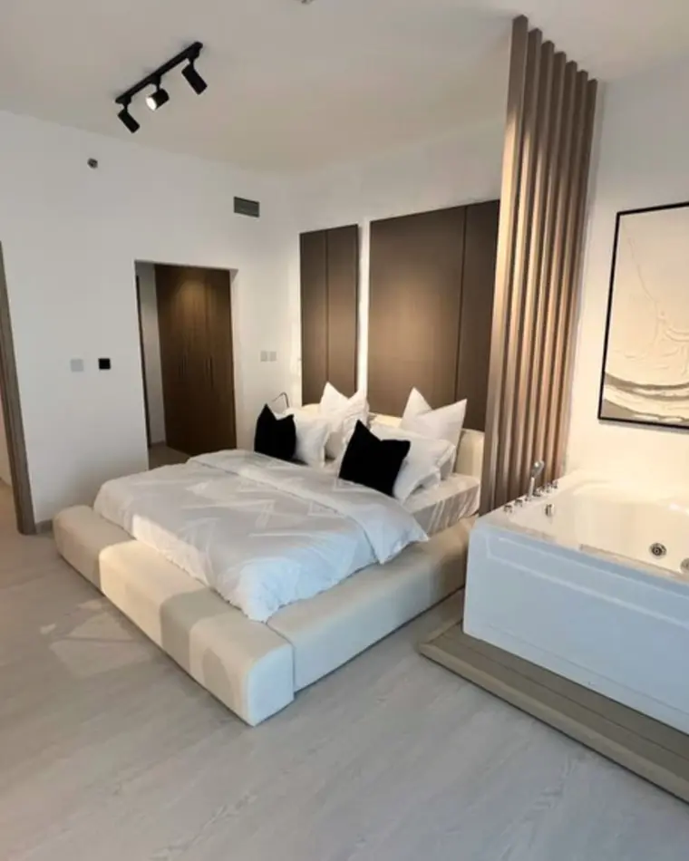 Bedroom in JVC: a bed alongside an inset jacuzzi, with track lighting and fluted panelling.