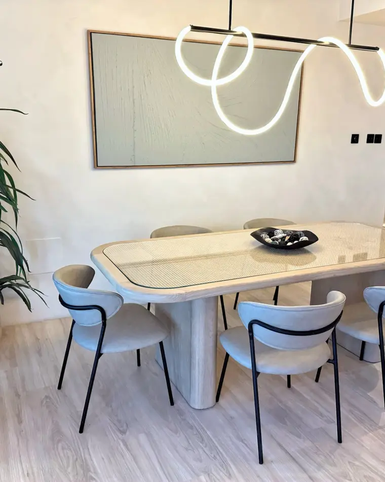 Dining room in TECOM: an oval table under a sculpted linear pendant, a large indoor plant and a framed canvas.