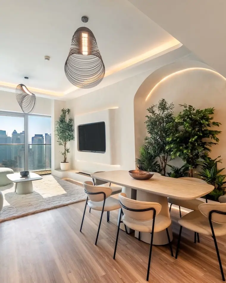 Dining room in Dubai Marina: an oval table under woven pendants, a planted plaster arch and a marina view.