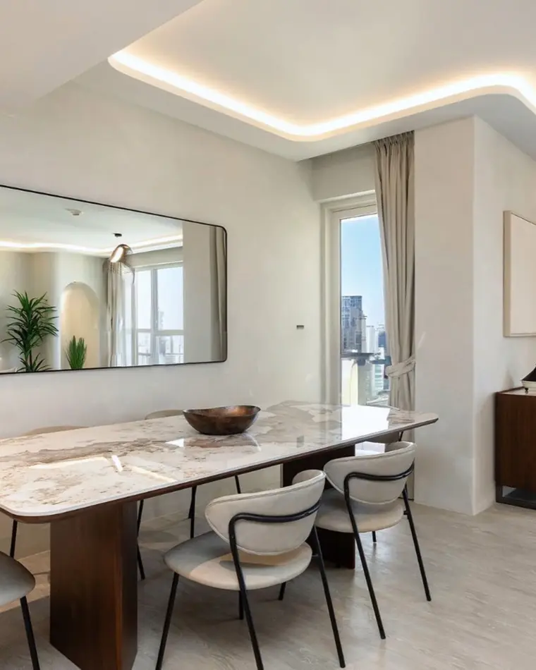 Dining room in JBR: a marble table with boucle chairs, a long mirror and a city view.