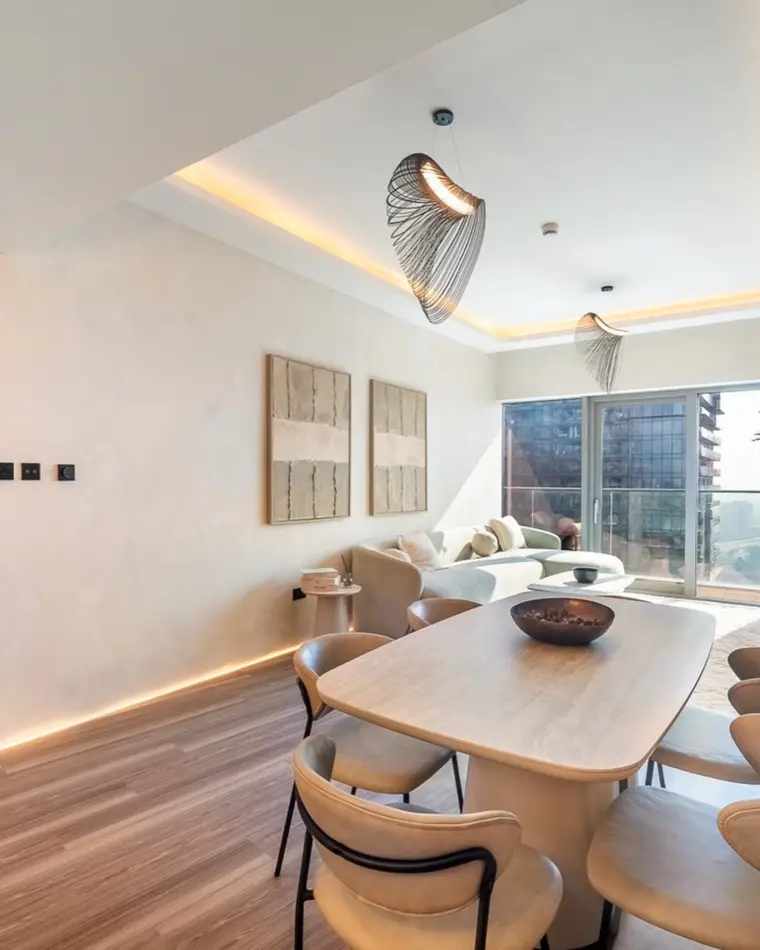 Dining room in Dubai Marina: an oval timber table under a woven pendant, with cove lighting and a balcony.