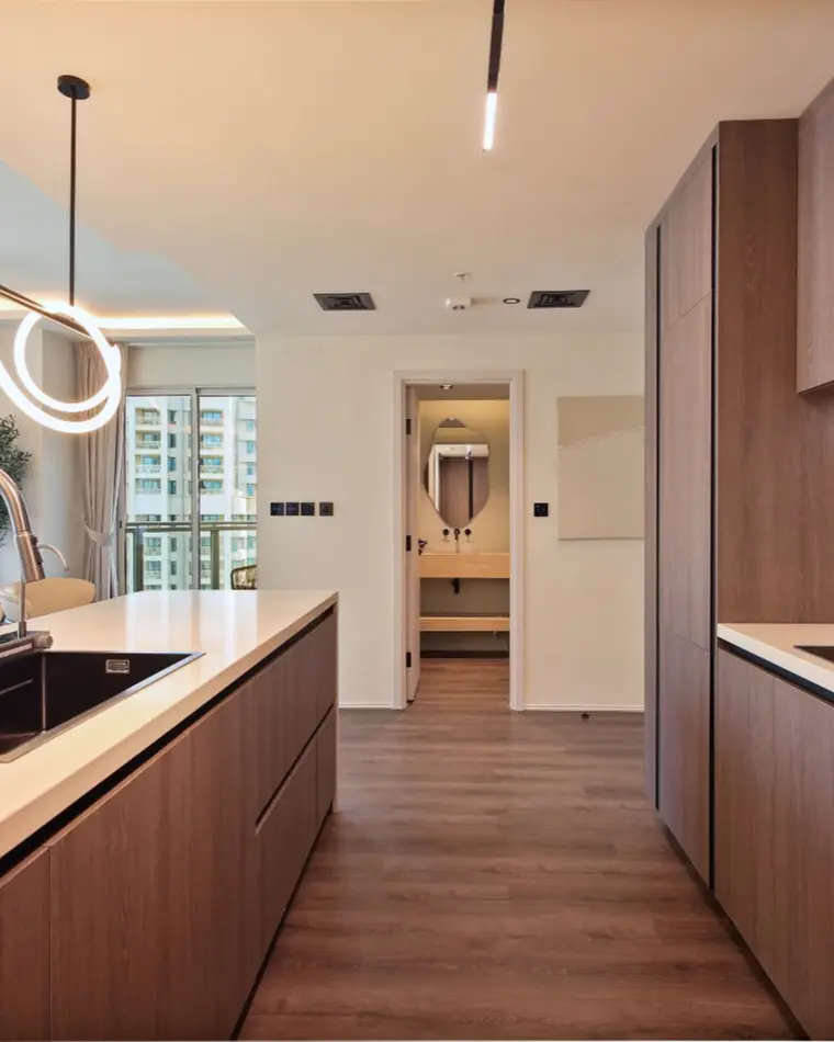 Kitchen in Downtown: walnut joinery to the ceiling, pale stone worktop, sculpted linear pendant over the island.