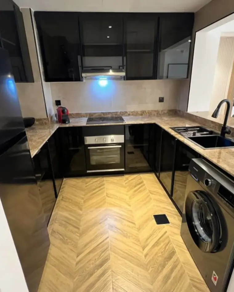 Kitchen in JVC: black gloss joinery, stone worktop and chevron oak flooring.