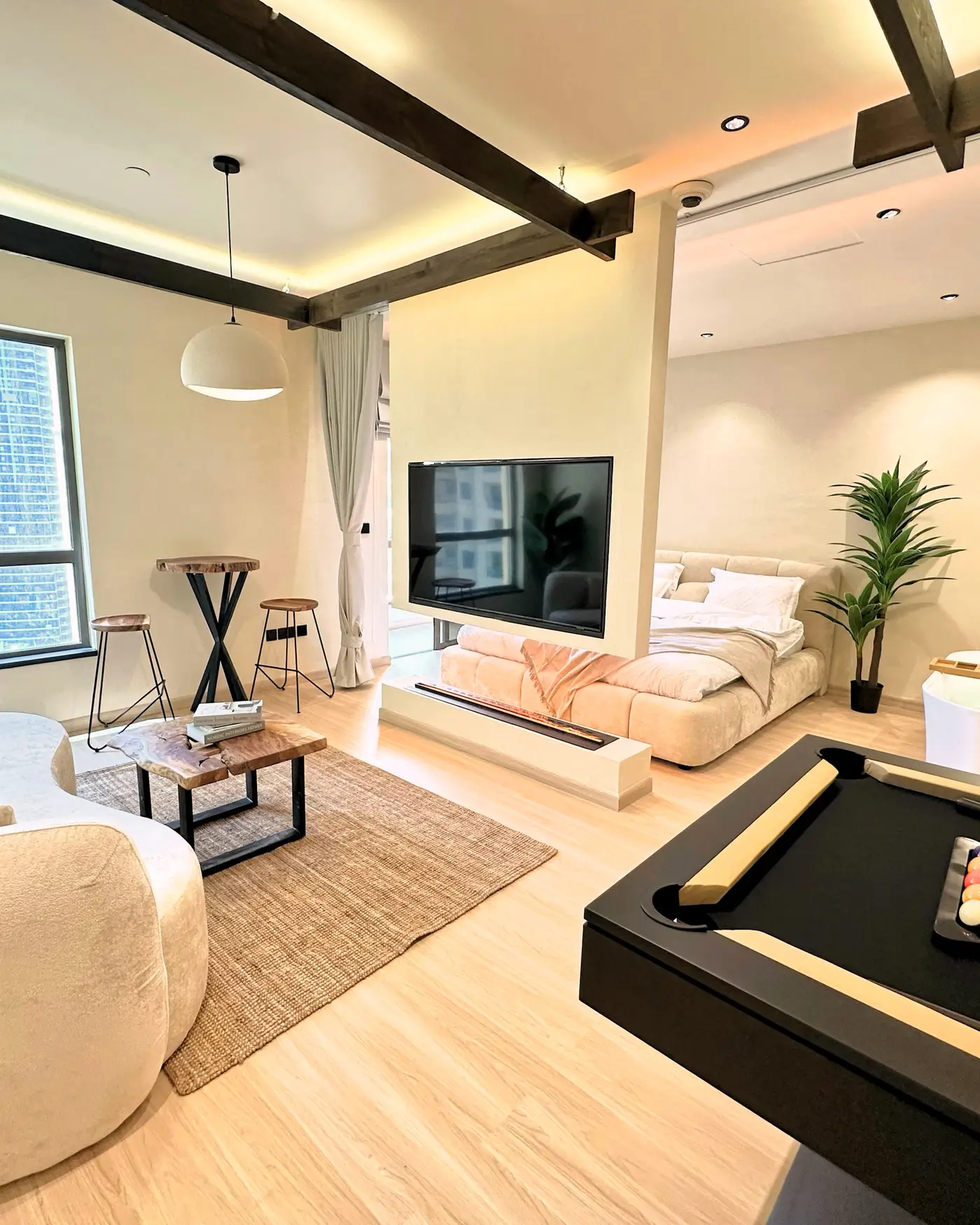 Living room in JBR: open floor with dark exposed beams, a pool table, curved boucle seating and pale oak flooring.