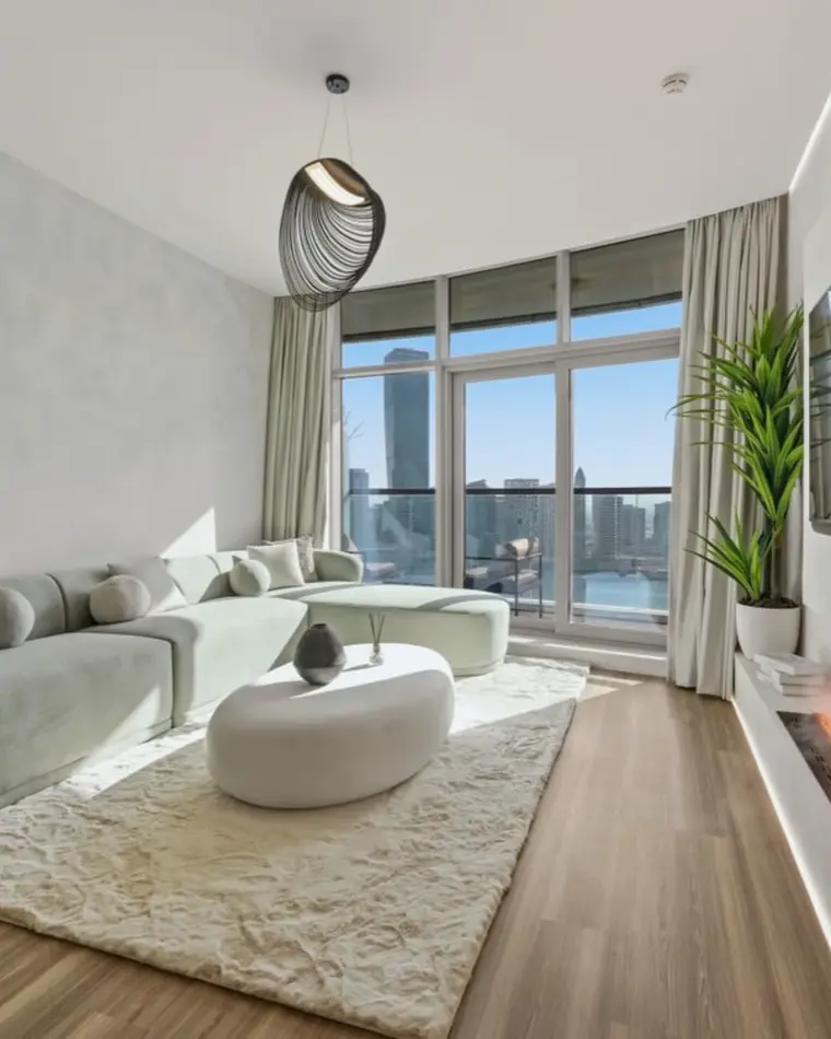 Living room in Business Bay: curved boucle sofa on a wool rug, a linear fireplace and full-height glazing onto the towers.