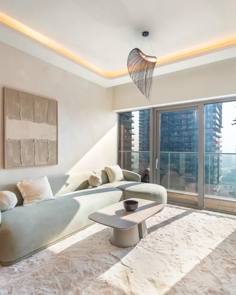 Living room in Dubai Marina: cream sofa, textured wall panels, an olive tree and a balcony onto the marina.
