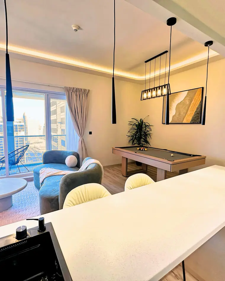 Living room in Business Bay: curved boucle sofa under dark beams, marina view through full-height glazing.