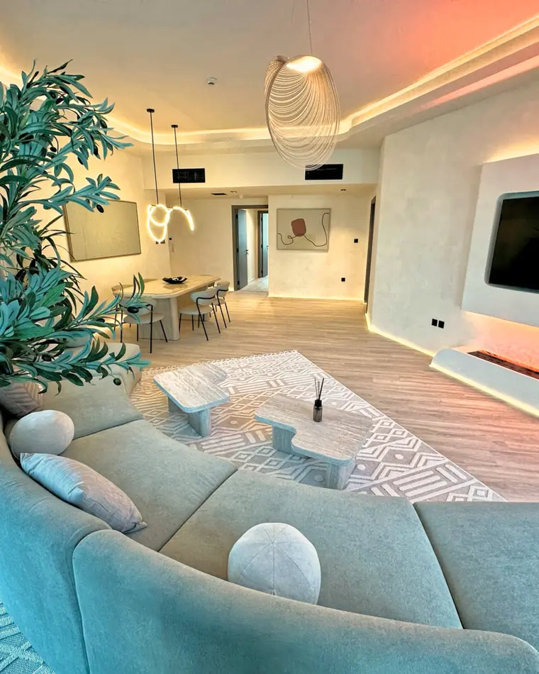 Living room in TECOM: pale sofa, track lighting, an olive tree and a recessed niche.