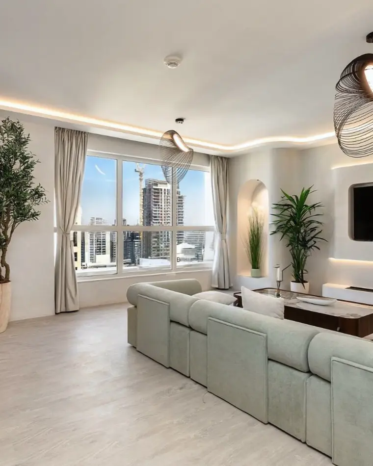 Living room in JBR: boucle armchairs around a stone coffee table, an olive tree and a window onto the lake.
