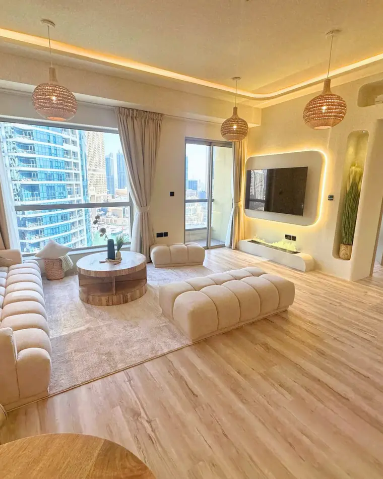 Living room in JBR: sage green sofa, olive trees, cove lighting and full-height glazing.