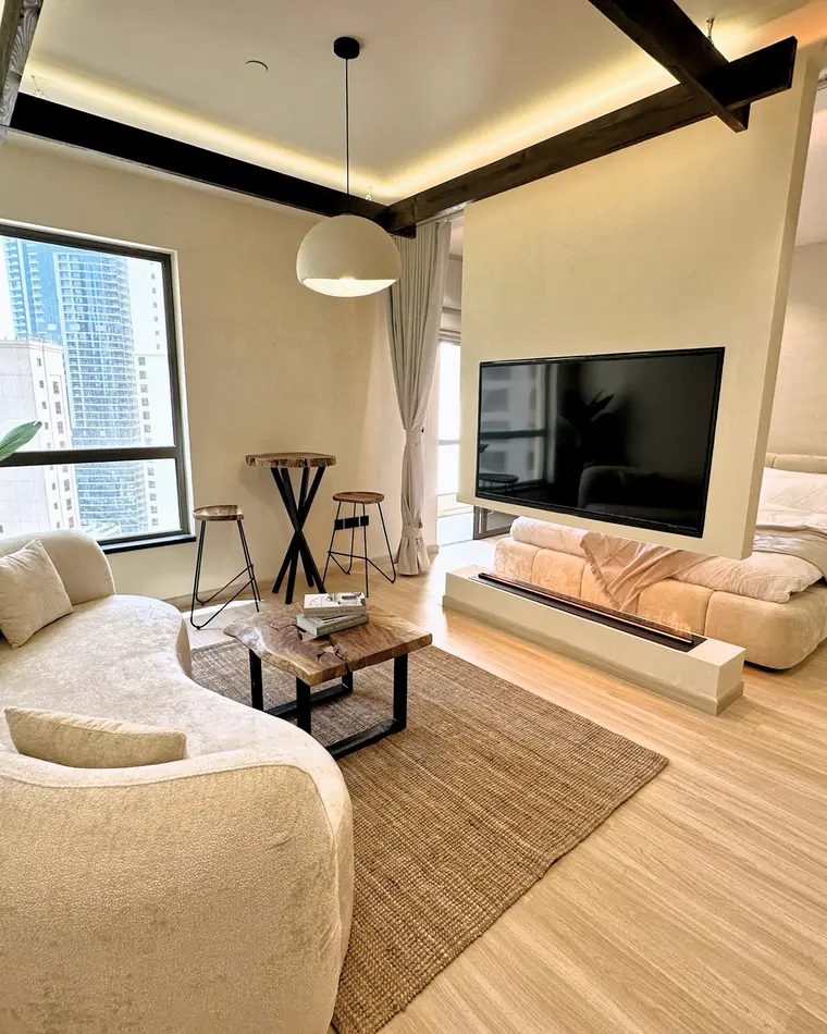 Living room in JBR: grey sofa, track lighting, a wall-mounted television and a niche wall.