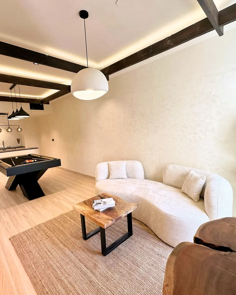 Living room in JBR: dark exposed beams, curved boucle sofa and a timber coffee table on a wool rug.