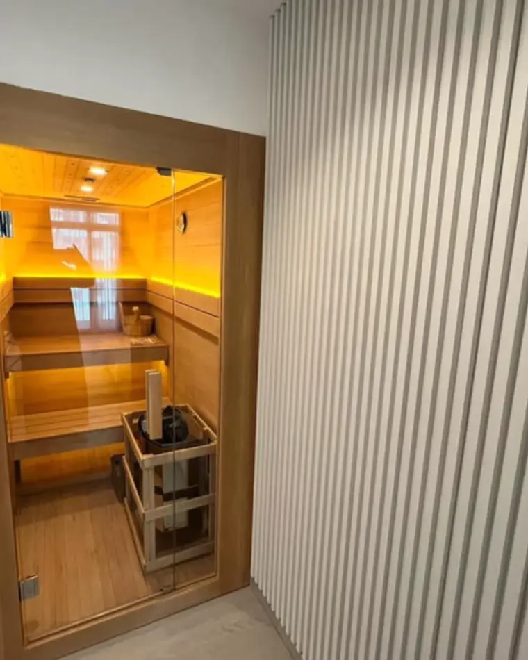 Sauna in JVC: a glazed sauna set into fluted panelling, with cedar benches inside.