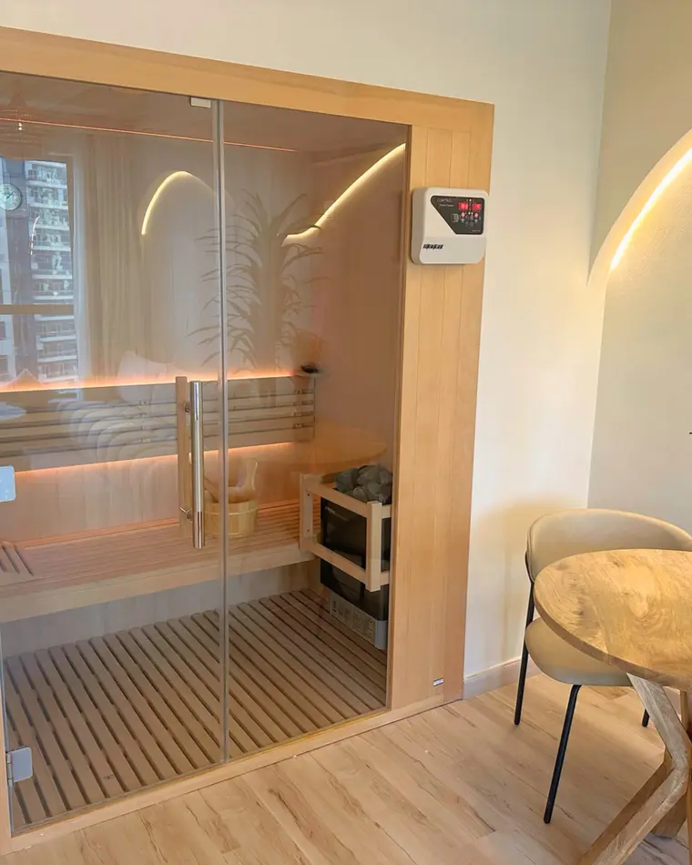 Sauna in JBR: a glazed sauna in an oak frame, beside a round table.